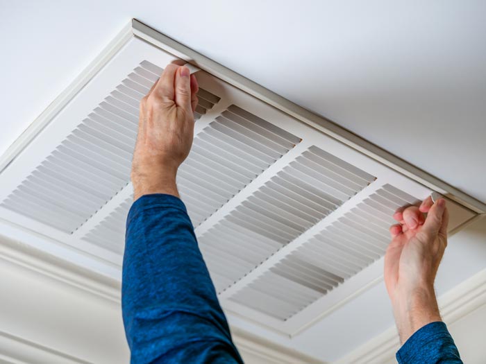Man opening ceiling air vent to replace dirty HVAC air filter