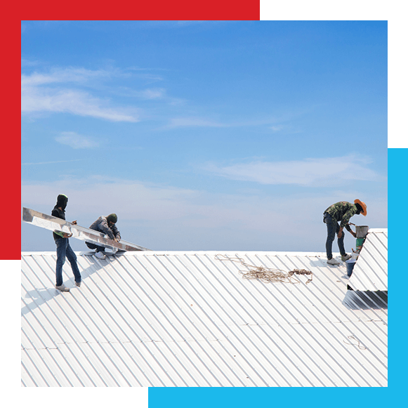 Workers repairing metal sheet roof under bright blue summer sky and light cloud. Long shot.
